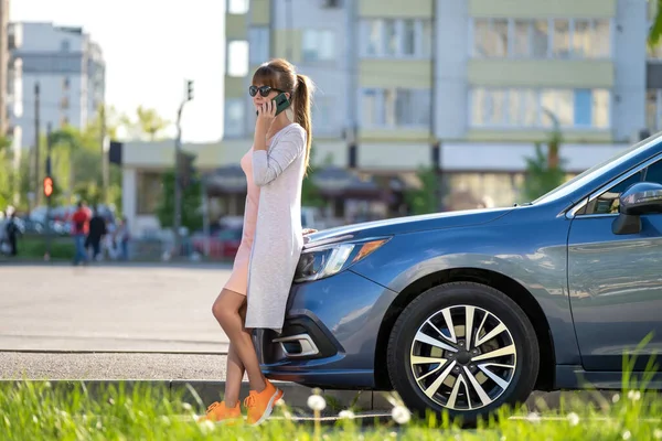 Joven conductora de pie cerca de su coche hablando por teléfono móvil en una calle de la ciudad en verano — Foto de Stock