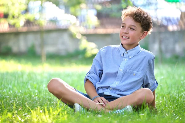 Молодий щасливий хлопчик відпочиває на зеленій траві в літньому парку. Позитивна дитина насолоджується літнім часом на відкритому повітрі. Концепція добробуту дітей — стокове фото