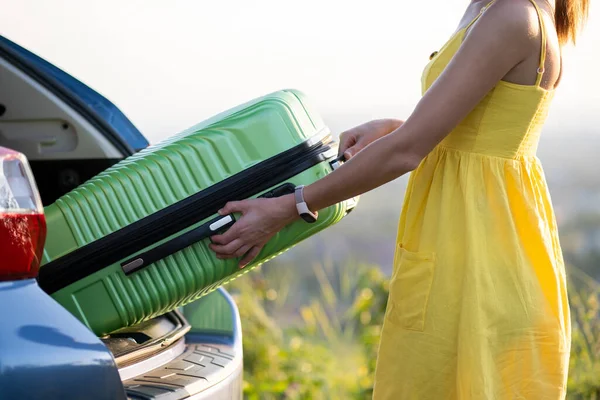 Junge Frau in gelbem Sommerkleid holt grünen Koffer aus dem Kofferraum. Reise- und Urlaubskonzept — Stockfoto