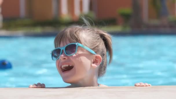 Ragazza felice bambino rilassante sul lato della piscina nella soleggiata giornata estiva — Video Stock