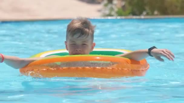 Retrato de niño feliz relajándose en círculo inflable en la piscina en el día soleado del verano durante las vacaciones tropicales. Concepto de actividades de verano — Vídeo de stock