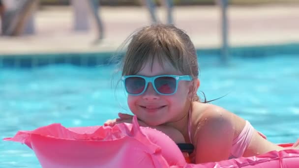 Молодая веселая девочка весело плавает на надувном надувном матрасе в бассейне с голубой водой в теплый летний день на тропических каникулах. Концепция летних мероприятий — стоковое видео