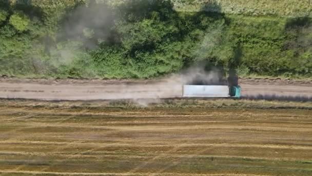 Vue aérienne de camion de fret conduisant sur la route de terre entre les champs de blé agricole faisant beaucoup de poussière. Transport du grain après récolte par moissonneuse-batteuse pendant la saison de récolte — Video