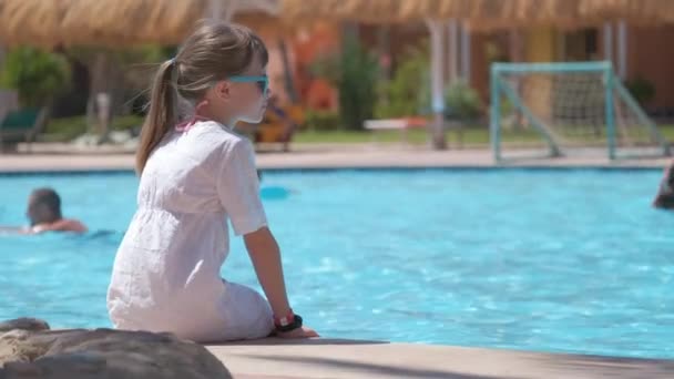 Portret szczęśliwej dziewczynki w białej sukience relaksującej się na basenie w słoneczny letni dzień podczas tropikalnych wakacji — Wideo stockowe