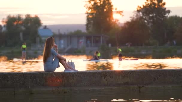 Vista lateral da mulher solitária sentada sozinha na margem do lago na noite quente. Solidão e relaxamento no conceito de natureza — Vídeo de Stock