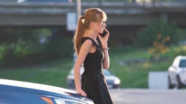 Jonge vrouwelijke bestuurder staan in de buurt van haar auto praten op mobiele telefoon in een stad straat in de zomer — Stockvideo