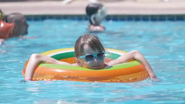 Ung glad barn flicka har roligt simma i uppblåsbara luft cirkel i poolen med blått vatten på varm sommardag på tropiska semestrar. Koncept för sommaraktiviteter — Stockvideo