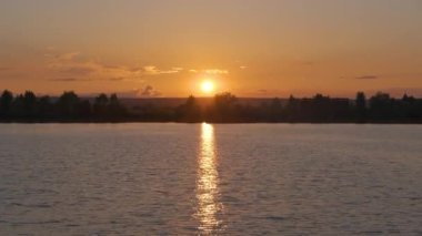 Göl suyunda kırılan park ağaçlarından oluşan karanlık bir siluet ve gün batımında parkın tepesinde yürüyen yayalar ile Lakeside manzarası