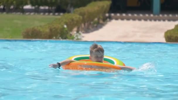 Счастливый мальчик плавал на кружке в бассейне в солнечный летний день во время каникул — стоковое видео