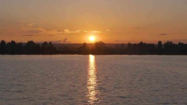 Lakeside τοπίο με σκούρα σιλουέτα από δέντρα πάρκο refliced στο νερό της λίμνης και μακρινούς πεζούς στο ανάχωμα κατά το φωτεινό ηλιοβασίλεμα — Αρχείο Βίντεο