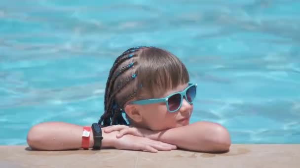 Молодая веселая девочка отдыхает на стороне бассейна с чистой голубой водой в солнечный летний день. Концепция тропического отдыха — стоковое видео