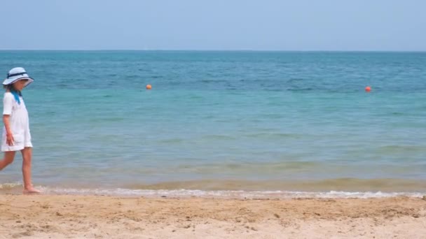 Glad barnflicka i vit sommarklänning promenader på stranden sandstrand under sommarsemestern. Resor och rekreation i semester koncept — Stockvideo