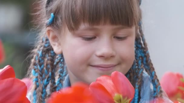 Menina feliz brincando no jardim de verão desfrutando de doce aroma de flores de tulipa vermelha no dia ensolarado — Vídeo de Stock