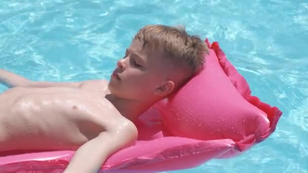 Niño alegre joven que se divierte nadando en el colchón inflable del aire en la piscina con el agua azul en el día caliente del verano en vacaciones tropicales. Concepto de actividades de verano — Vídeo de stock