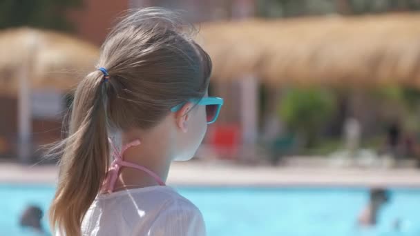 Jovem menina alegre descansando no lado da piscina com água azul clara no dia ensolarado de verão. Conceito de férias tropicais — Vídeo de Stock