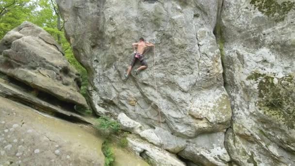 Joven escalando empinada pared de montaña rocosa. Hombre escalador supera ruta desafiante. Participar en el concepto de deporte extremo — Vídeo de stock