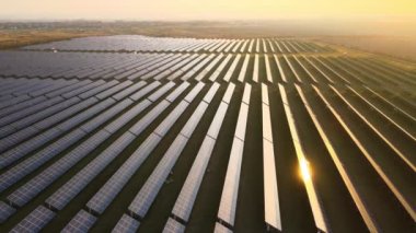 Günbatımında temiz elektrik enerjisi üretmek için birçok sıra güneş fotovoltaik paneli bulunan sürdürülebilir büyük elektrik santralinin havadan görünüşü. Sıfır emisyon kavramı ile yenilenebilir elektrik