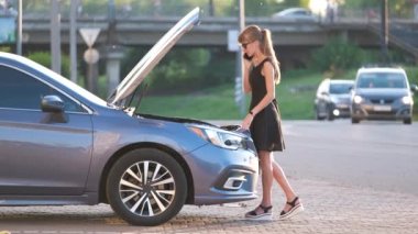Kaputu açık bir şekilde arabasının yanında duran çaresiz kadın yardım için yol servisini arıyor. Genç bayan sürücünün aracıyla ilgili sorunları var