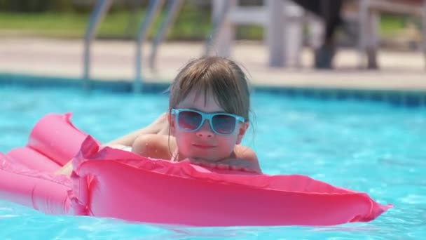 夏の太陽の下でリラックスした若い女の子は、熱帯の休暇中にプールで膨脹可能な空気マットレスで泳ぐ。夏のアクティビティコンセプト — ストック動画