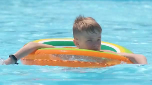 Glad pojke simmar på uppblåsbar cirkel i poolen på solig sommardag under tropiska semestrar — Stockvideo