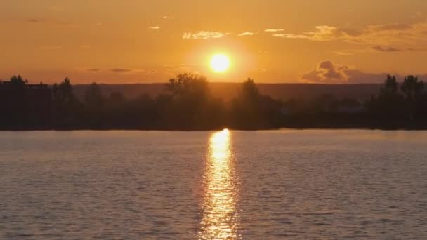 Lakeside landschap met donker silhouet van park bomen weerspiegeld in meer water en ver lopen voetgangers op dijk bij heldere zonsondergang — Stockvideo