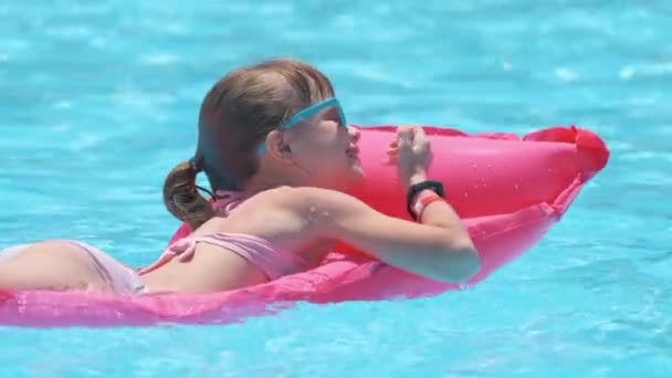 Νεαρό χαρούμενο κορίτσι που διασκεδάζει κολυμπώντας σε φουσκωτό στρώμα αέρα στην πισίνα με μπλε νερά τη ζεστή καλοκαιρινή μέρα στις τροπικές διακοπές. Έννοια των καλοκαιρινών δραστηριοτήτων — Αρχείο Βίντεο