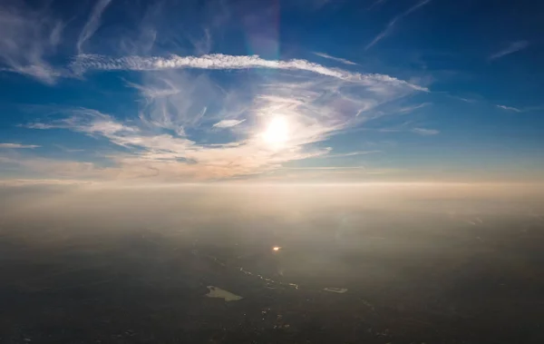 Vue aérienne depuis la fenêtre de l'avion à haute altitude de la ville recouverte d'une fine couche de smog brumeux et de nuages lointains le soir — Photo