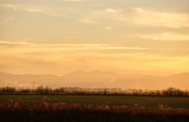 Güzel bir akşam panoramik manzarası. Gün batımında güneş batarken uzak dağ tepeleri ve asfalt yolda batıyor.