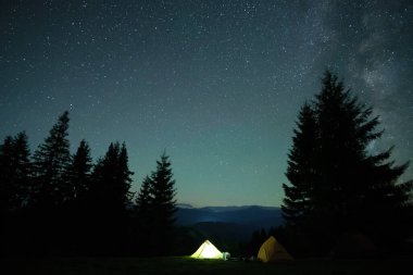 Parlak turist çadırları gece gökyüzünün altındaki karanlık dağlarda parlayan parlayan yıldızlarla. Etkin yaşam tarzı kavramı