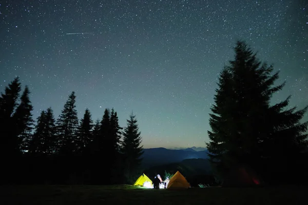 Tentes de camping lumineuses qui brillent sur le camping dans les montagnes sombres sous le ciel étoilé couvert de nuit. Style de vie actif et concept de voyage — Photo