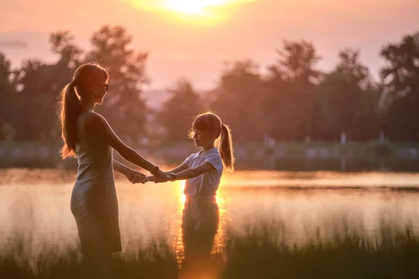 Glückliche Mutter und Tochter stehen Hand in Hand und genießen die Zeit im Sommerpark am Abend. Familienliebe und Beziehungskonzept — Stockfoto