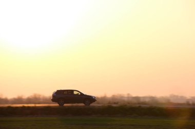 Gün batımında şehirlerarası yolda hızla giden bir SUV arabası. Akşamları otoyol trafiği