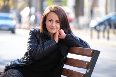 Genç ve mutlu bir kadın sıcak bir sonbahar gününde şehir bankında dinleniyor. İyi olmak ve günlük acele konseptinden dinlenmek