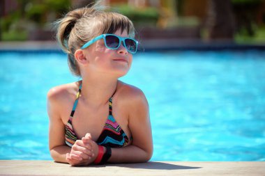 Neşeli genç kız güneşli yaz gününde açık mavi suyla havuz kenarında dinleniyor. Tropik tatil kavramı