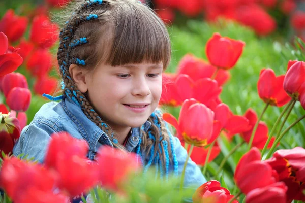 Glad barn flicka njuter söt lukt av röda tulpan blommor i sommar trädgård — Stockfoto