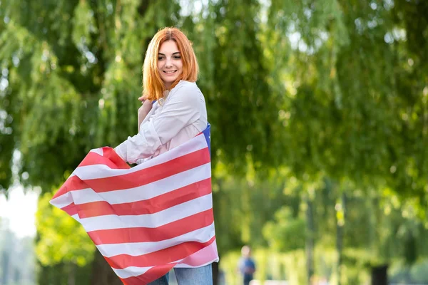 Joyeux jeune femme posant avec le drapeau national des États-Unis debout à l'extérieur dans le parc d'été. Fille positive avec bannière États-Unis à l'extérieur — Photo