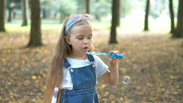 Petite fille heureuse enfant soufflant des bulles de savon à l'extérieur dans un parc vert. Concept d'activités d'été en plein air — Photo