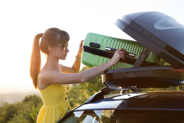 Junge Fahrerin legt grünen Koffer in Autodachträger Reise- und Urlaubskonzept — Stockfoto