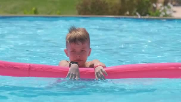 Niño feliz que se relaja en el colchón inflable del aire en la piscina en día soleado del verano durante vacaciones tropicales. Concepto de actividades de verano — Vídeo de stock