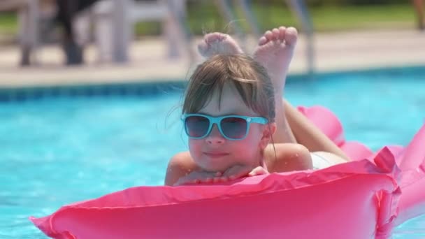 Young joyful child girl having fun swimming on inflatable air mattress in swimming pool with blue water on warm summer day on tropical vacations. Summertime activities concept — Stock Video