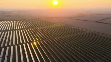 Günbatımında temiz elektrik enerjisi üretmek için birçok sıra güneş fotovoltaik paneli bulunan sürdürülebilir büyük elektrik santralinin havadan görünüşü. Sıfır emisyon kavramı ile yenilenebilir elektrik