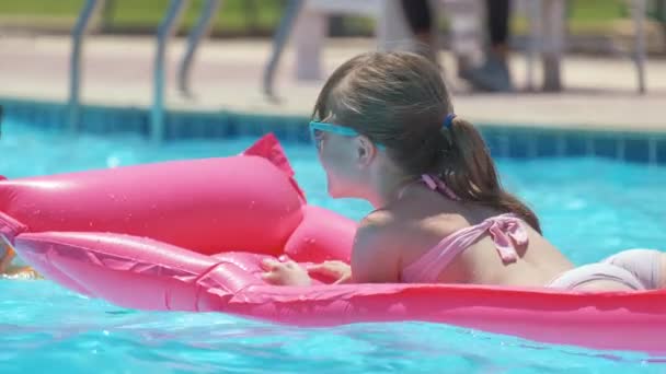 열대 지방에서 휴가를 보내는 어느 화창 한 여름날 수영장에서 푹신푹신 한 공기 매트리스를 신고 휴식을 취하는 행복 한 소녀. 여름 활동 개념 — 비디오