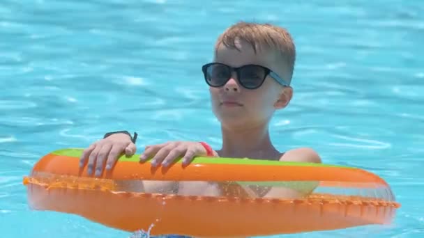 Gelukkig kind jongen zwemmen op opblaasbare cirkel in het zwembad op zonnige zomerdag tijdens tropische vakanties — Stockvideo