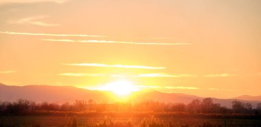 Güzel bir akşam panoramik manzarası. Gün batımında güneş batarken uzak dağ tepeleri ve asfalt yolda batıyor.