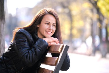 Sıcak bir sonbahar gününde, teneffüste sokak bankında boş vakit geçiren mutlu genç bir kadın. Günlük koşuşturma konseptinin rahatlığı ve dinlenmesi