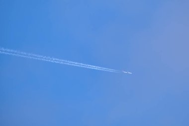 Mesafeli yolcu jet uçağı açık mavi gökyüzünde yüksek irtifada uçarken ardında beyaz duman izi bırakıyor. Hava taşımacılığı kavramı