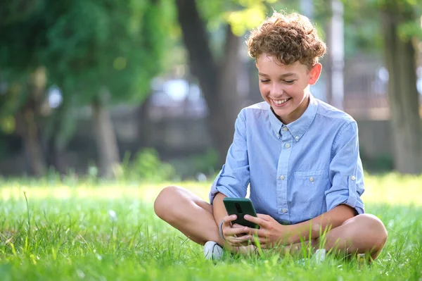 Niño navegando por su teléfono inteligente al aire libre en el parque de verano. Uso del teléfono móvil para el arrendamiento y el concepto de educación — Foto de Stock