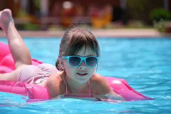 Маленькая девочка отдыхает на летнем солнце, купаясь на надувном воздушном матрасе в бассейне во время тропических каникул. Концепция летних мероприятий — стоковое фото