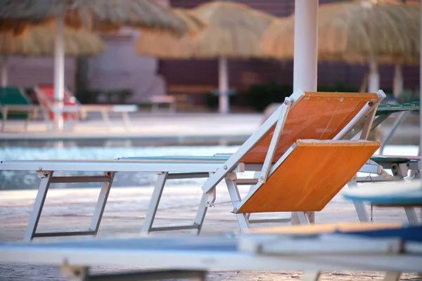 Lege ligstoelen onder stroschaduwparasols aan de rand van het zwembad in tropisch resort. Zomervakantie en vluchtconcept — Stockfoto