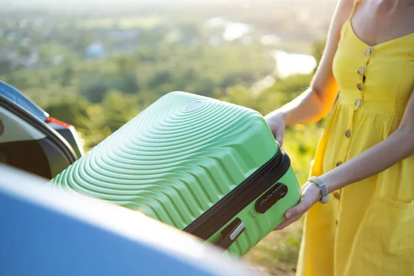 Großaufnahme von Frauenhänden, die grüne Koffer aus dem Kofferraum holen. Reise- und Urlaubskonzept — Stockfoto